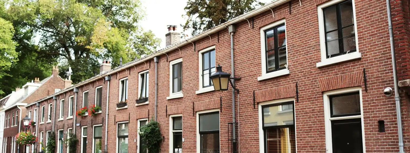 A terrace of red-brick Dutch houses with white window frames along a quiet street